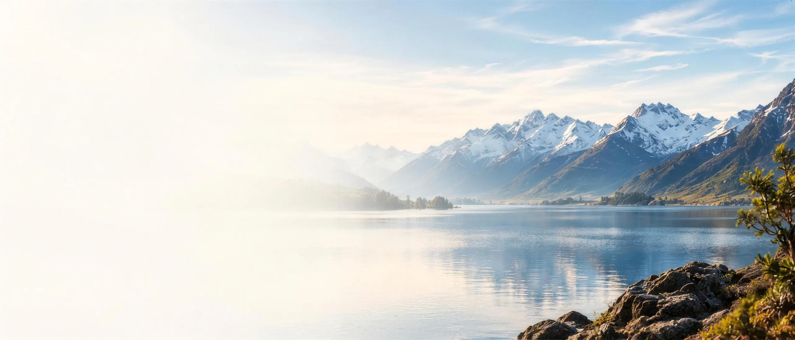 A still New Zealand glacial lake reflecting snow-capped mountains and beech forest at golden hour